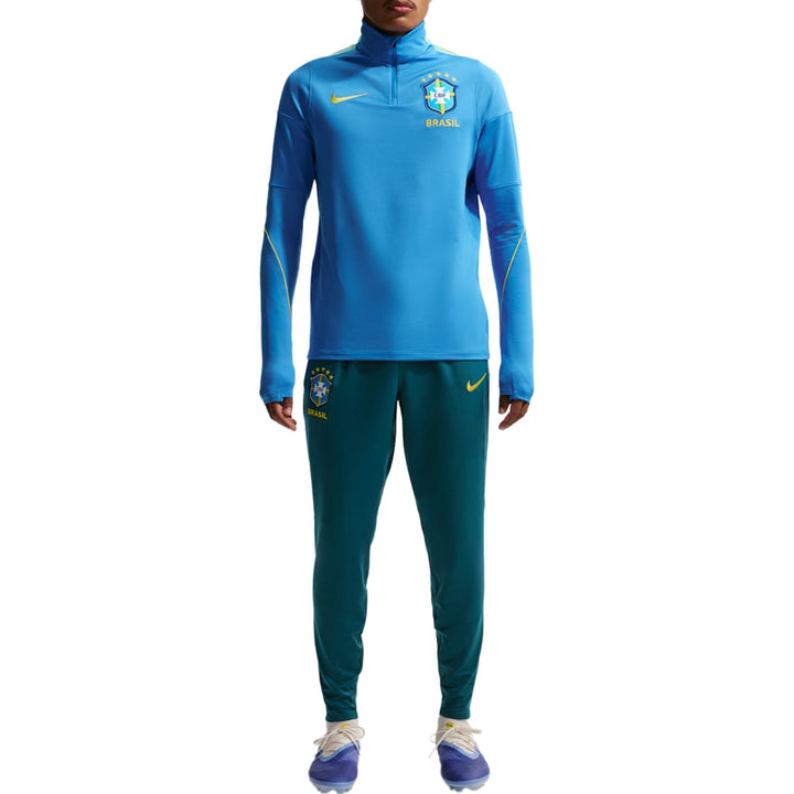 Blue Nike tracksuit with long sleeves and zip collar, featuring Brazil national team logo and green pants.