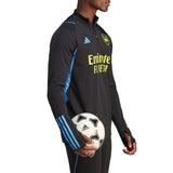 2023 24 Arsenal football tracksuit set black and blue with Emirates sponsor logo worn by male model holding soccer ball