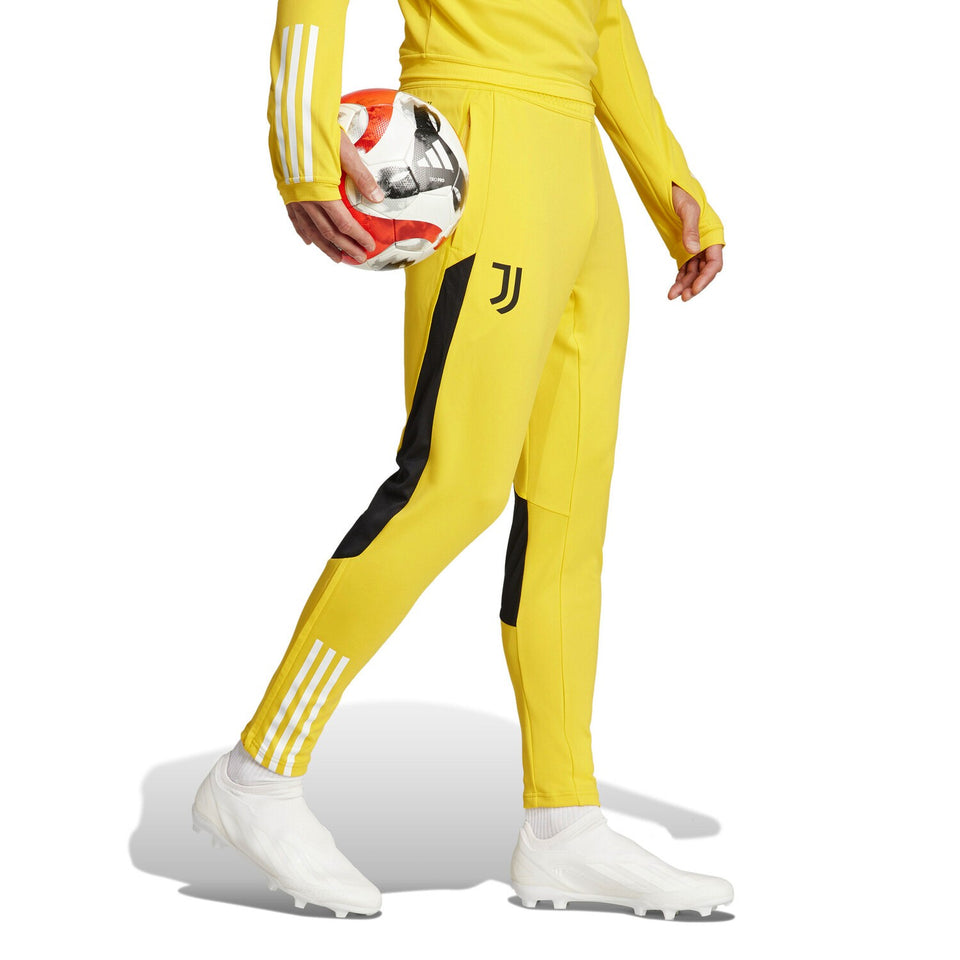 Juventus yellow training tracksuit 2024 pants with black accents and white cleats holding a soccer ball
