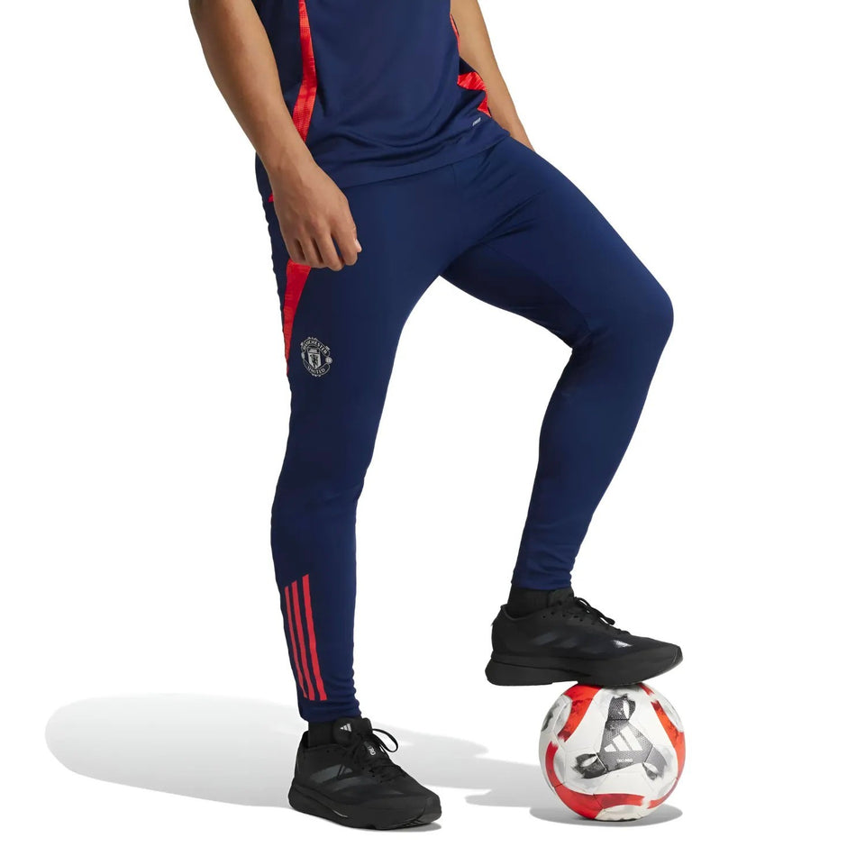 Navy blue Manchester United 2024 training tracksuit pants with red accents and black sports shoes
