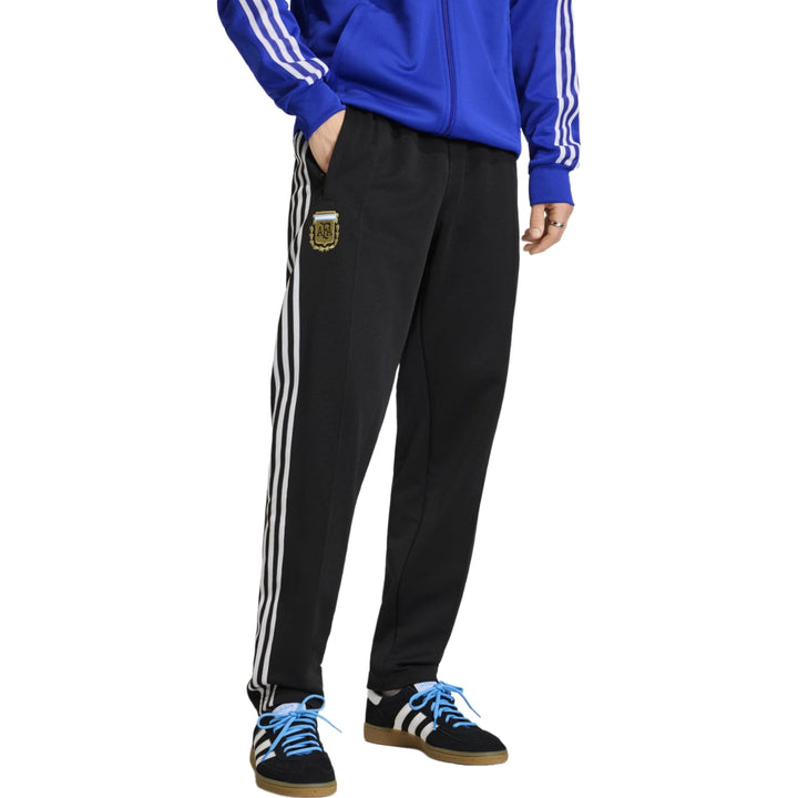 Black athletic pants with white stripes and gold logo from Adidas, designed for casual wear.