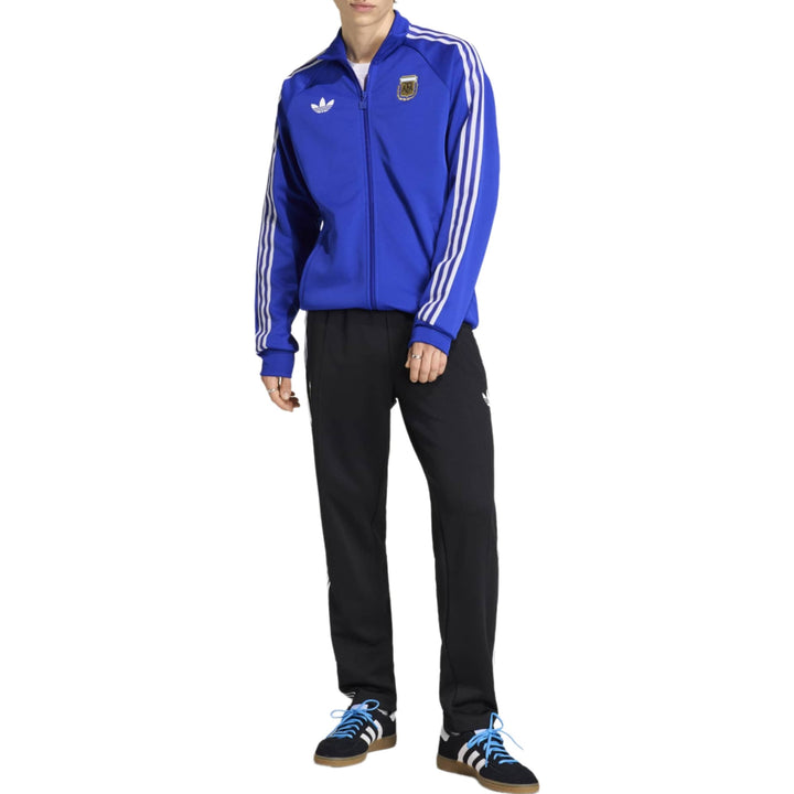 Blue Adidas tracksuit jacket with white stripes and logo, paired with black track pants.