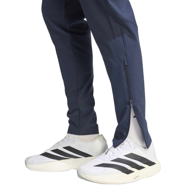 Navy athletic pants with zippered cuffs and white Adidas running shoes with black stripes.
