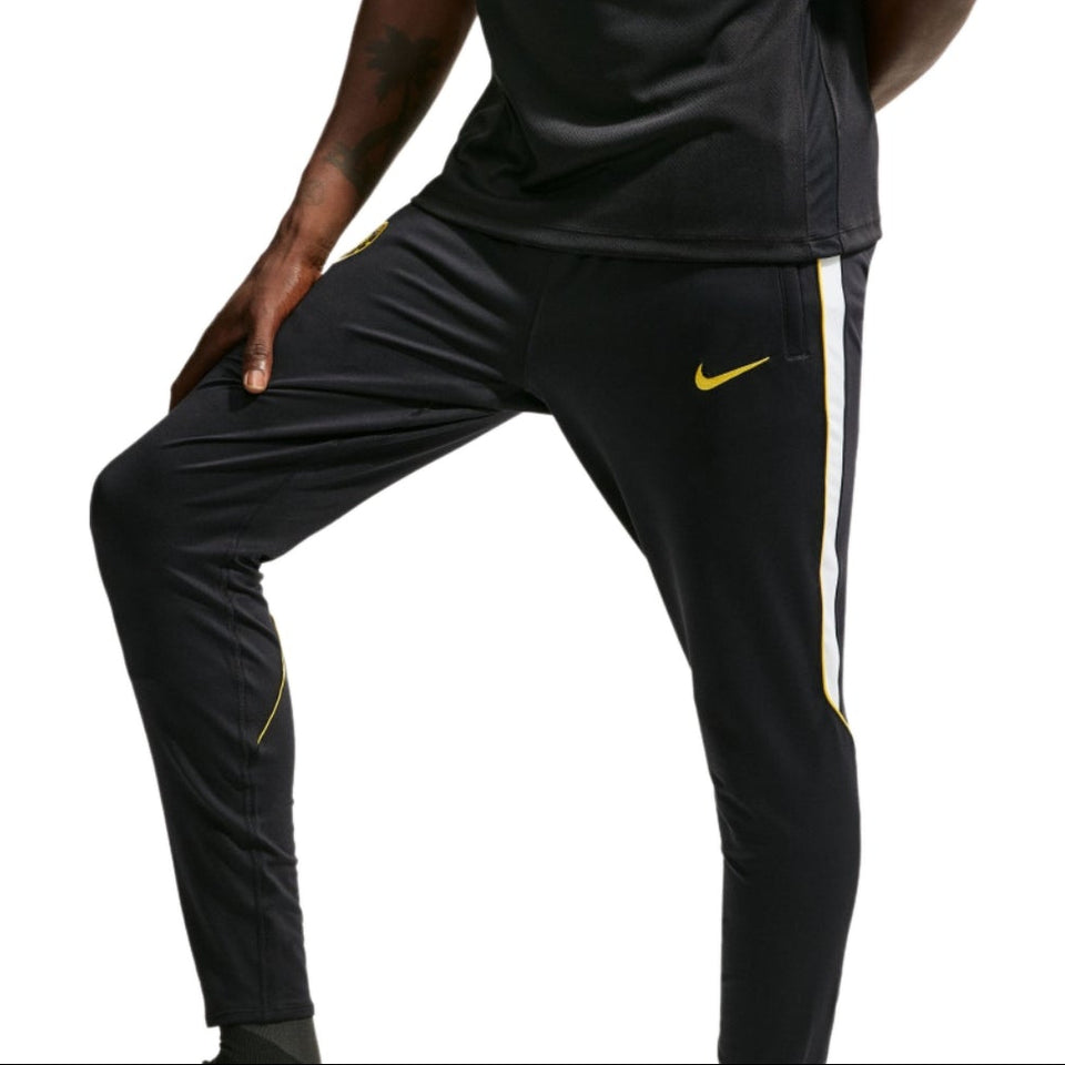 A man wearing a black Nike Chelsea FC training kit with yellow accents, featuring a short-sleeve top with a 'Bingx' sponsor logo and matching track pants, set against a plain white background.