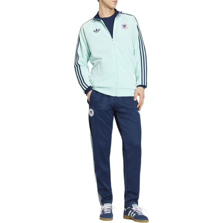 Mint green Adidas track jacket with navy pants featuring three stripes and logo details.