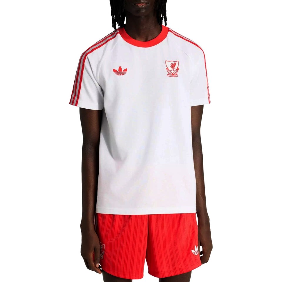 Person wearing a Liverpool FC x Adidas Originals white t-shirt with red accents and red shorts, featuring Adidas logos.