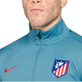 Close-up of Atletico Madrid soccer tracksuit for sale with team crest and red Nike logo on teal jacket