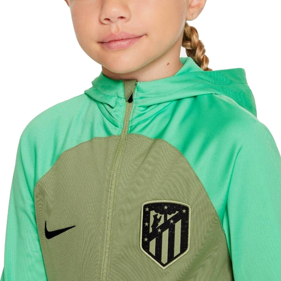 Close-up of kids Atletico Madrid tracksuit on SoccerTracksuits.com in green with hood and logo patch