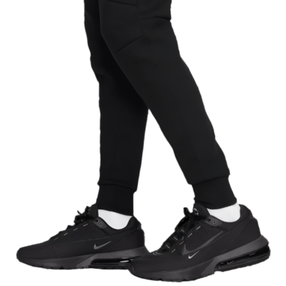 Model wearing Liverpool FC black tech fleece pants with tapered cuffed ankles paired with black Nike sneakers