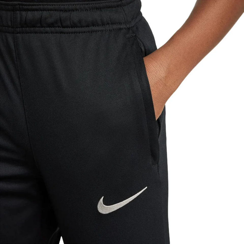 Close-up of black official kids Nike Barca tracksuit pants with white Nike logo and hand in pocket