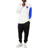 Man wearing PSG Nike Total 90 tracksuit 2025 26 white jacket with blue sleeve and black pants with red Nike swoosh
