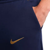 Close-up of navy blue Nike tech fleece tracksuit France 2024 pants with gold Nike logo and hand in pocket