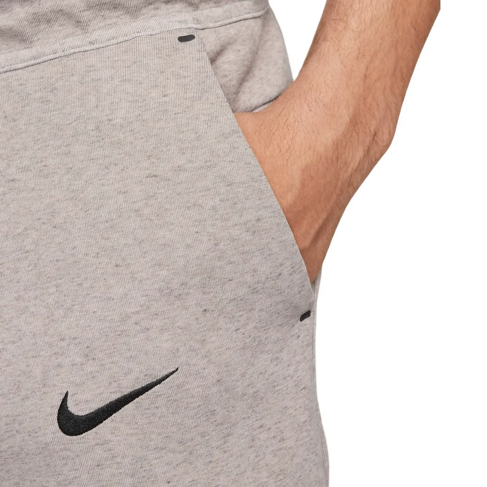 Close-up of gray Tottenham Hotspur Tech Fleece tracksuit pants with black Nike logo and hand in pocket