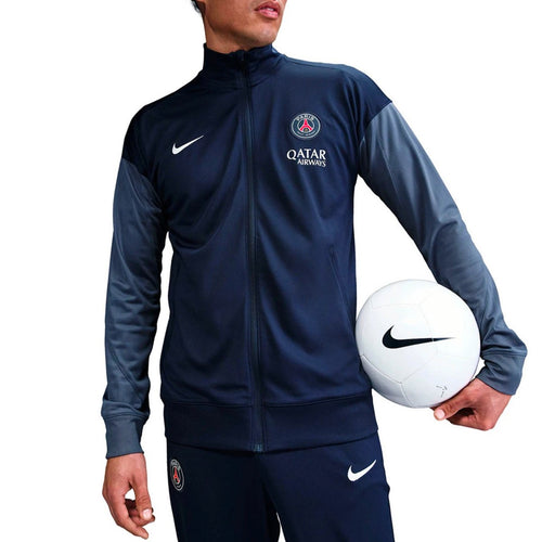 Model wearing Paris Saint-Germain 2025 soccer tracksuit with Nike logo and holding a soccer ball