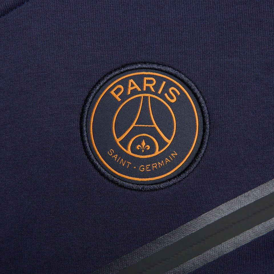 Close-up of Paris Saint-Germain logo on navy PSG tech fleece tracksuit 2023 with grey stripes