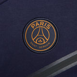 Close-up of Paris Saint-Germain logo on navy PSG tech fleece tracksuit 2023 with grey stripes