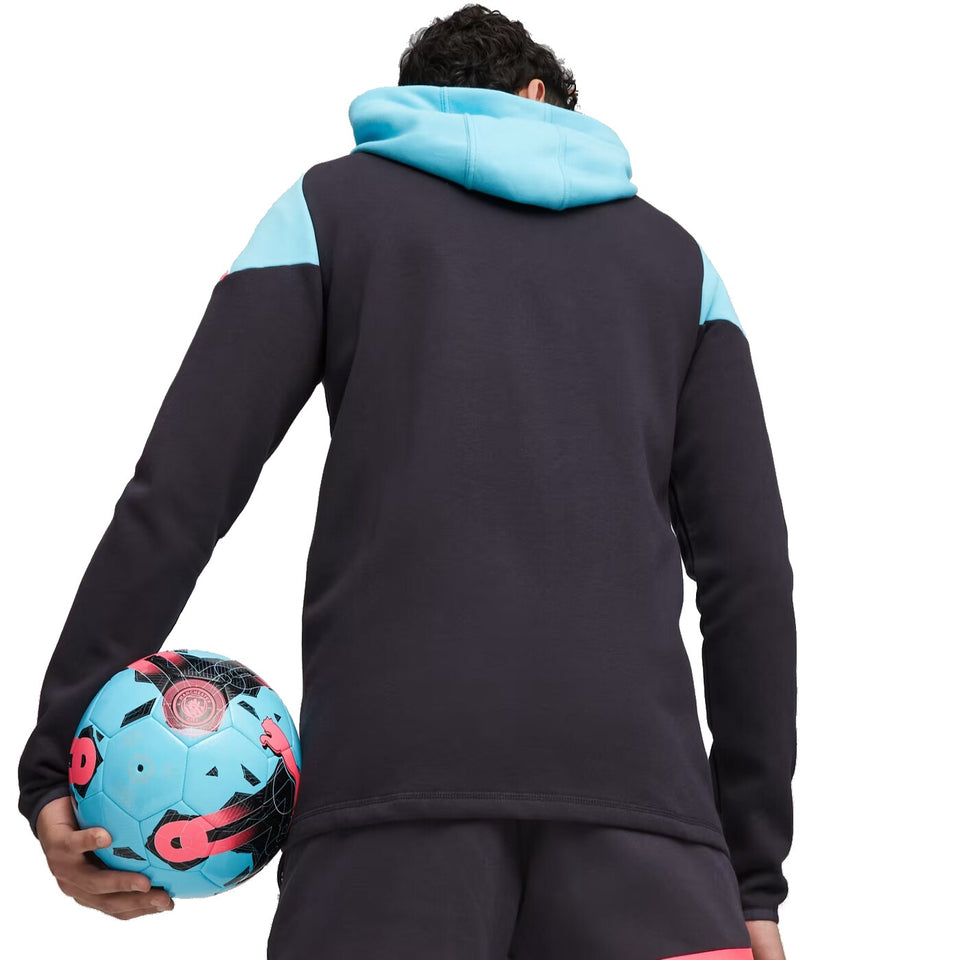 Back view of man wearing Puma Man City hooded tracksuit holding blue and black soccer ball