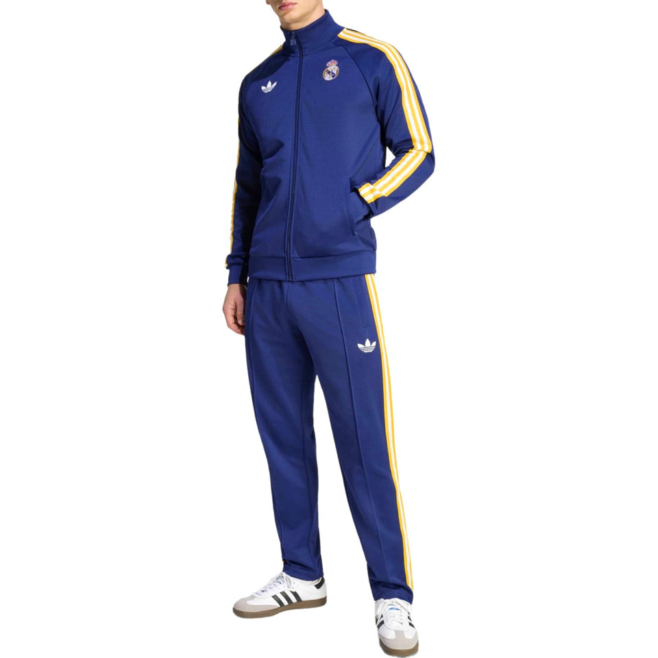 Person wearing a blue Adidas Originals x Real Madrid tracksuit with yellow stripes on a white background