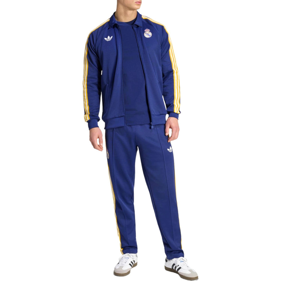 Person wearing a navy blue Adidas Originals x Real Madrid and yellow tracksuit with Adidas logo on a white background