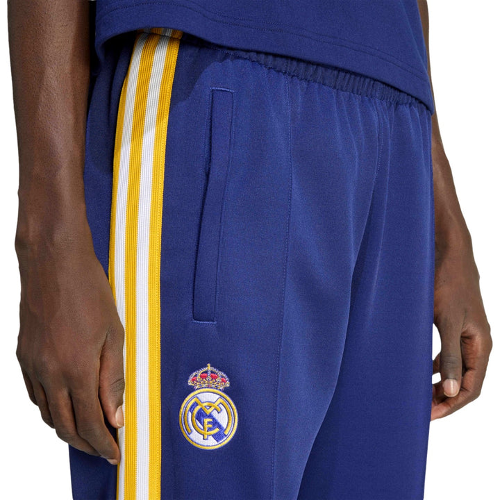 Blue Adidas Originals x Real Madrid pants with yellow and white stripes featuring a logo on a white backgrond
