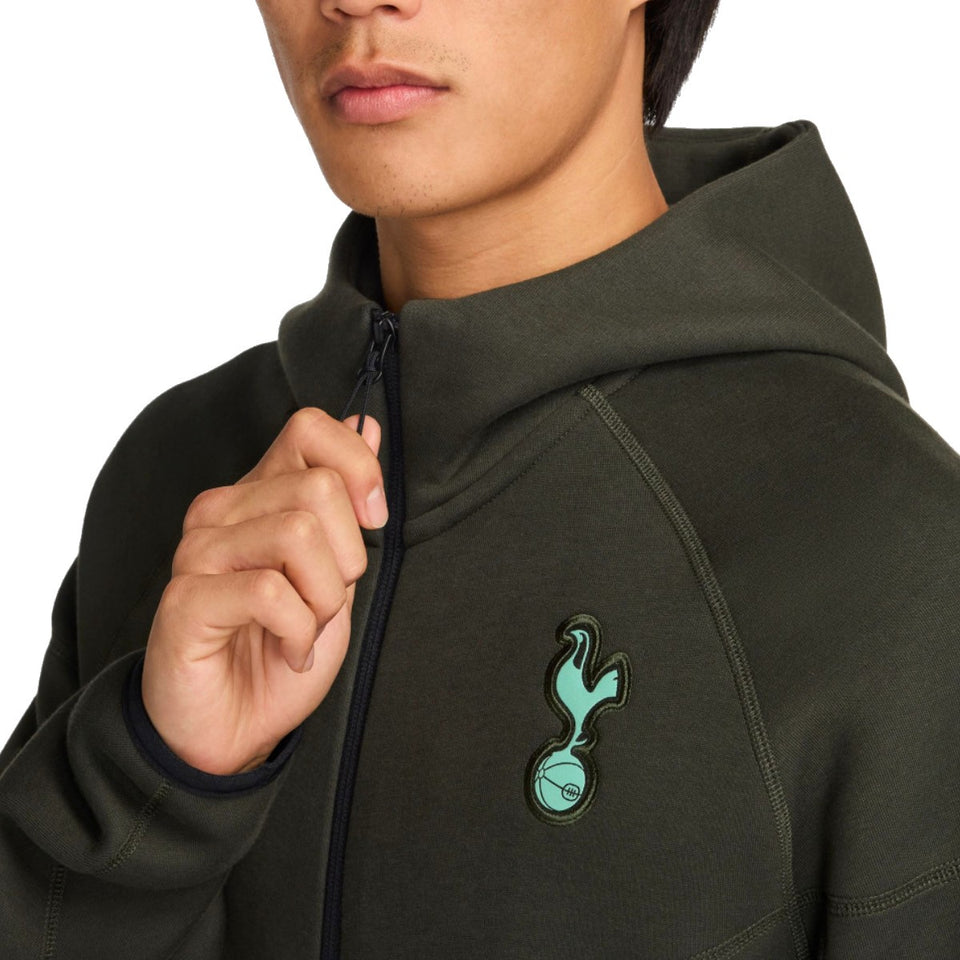 Close-up of a man wearing a dark green Tottenham Hotspur Nike Tech Fleece tracksuit jacket with zipped collar