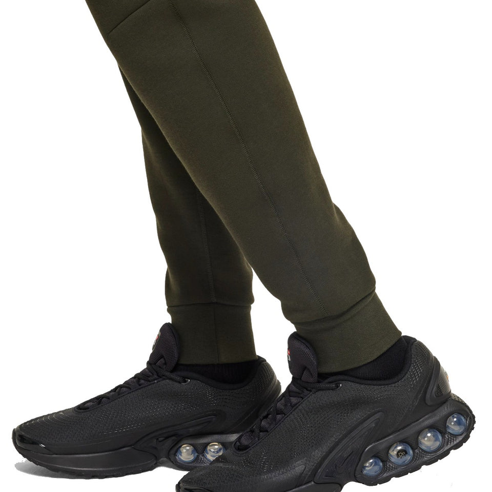 Close-up of legs wearing black sneakers and olive green pants from Tottenham Hotspur Nike Tech Fleece tracksuit