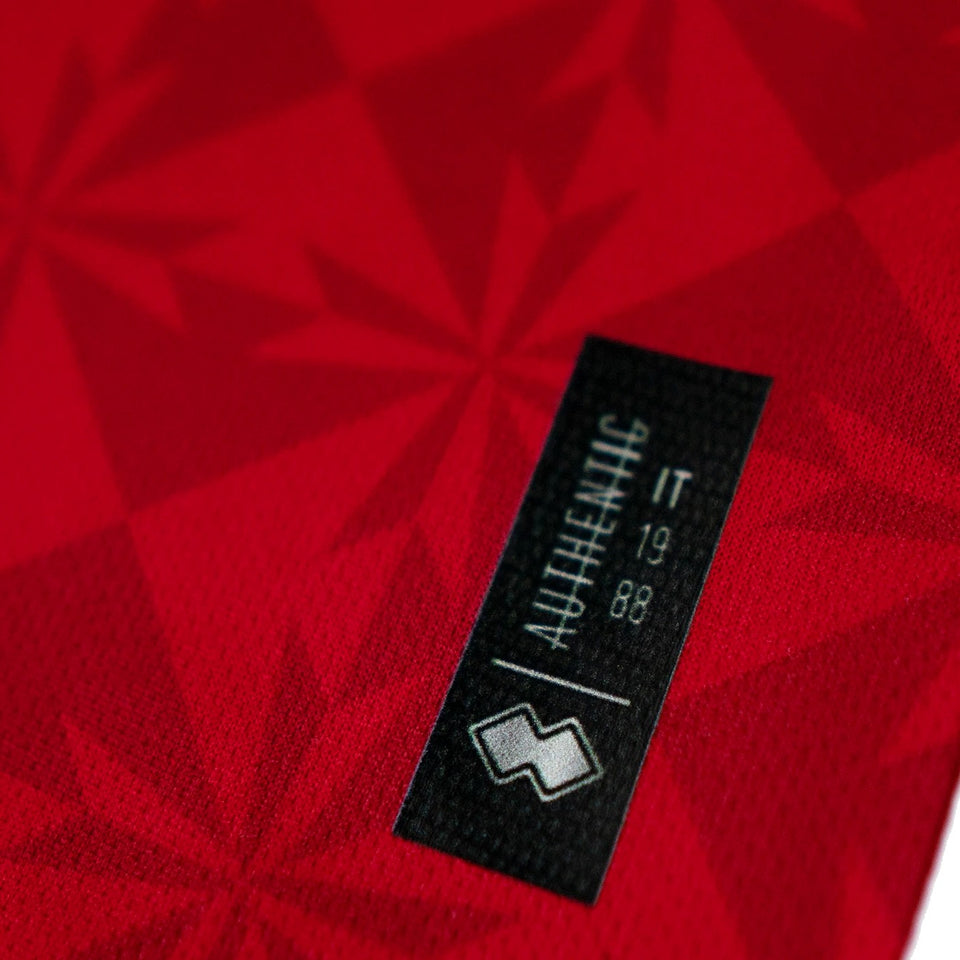 Close-up of the Malta national soccer jersey 2022 tag displaying authenticity details in red fabric